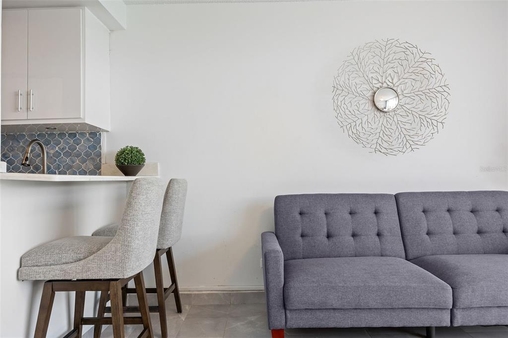 A gray sofa sits next to a kitchen counter with two bar stools and tile backsplash — 1477 ASHFORD UNIT 608, SAN JUAN, PR