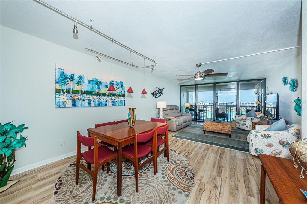 A dining area and living room with wood-look flooring, a ceiling fan, and balcony access — 9525 BLIND PASS ROAD UNIT 505, ST PETE BEACH, FL
