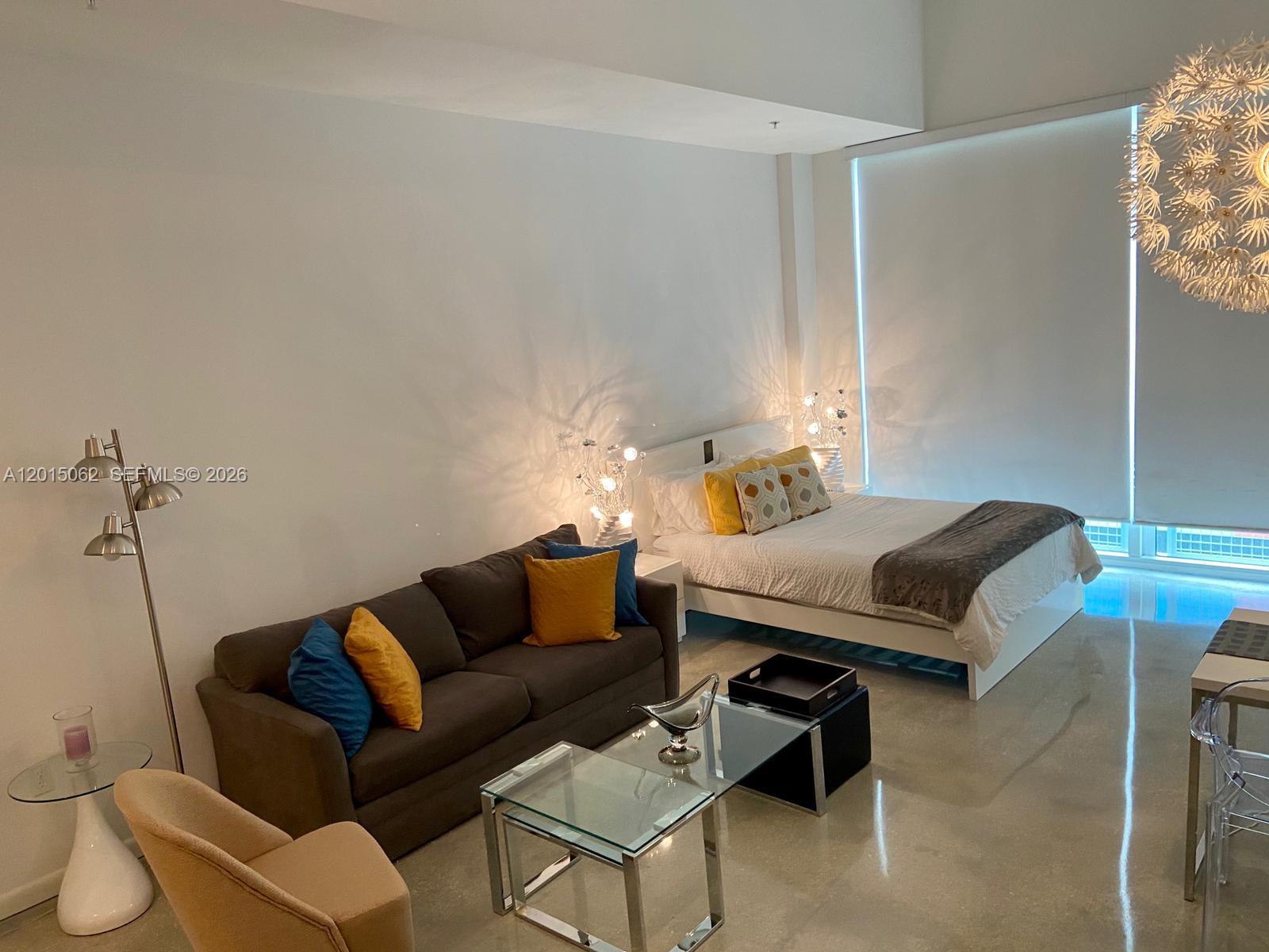 A studio apartment features a bed, a gray sofa, a glass coffee table, and lighting — 253 NE 2nd St # 312, Miami FL 33132, MIAMI, FL