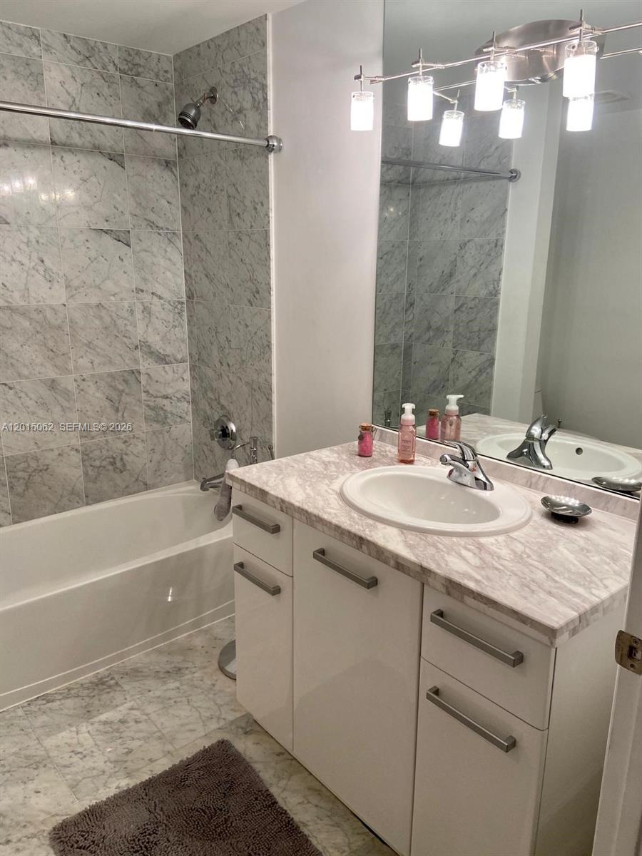 A bathroom features a marble-tiled shower, a white vanity with a marble countertop, and lighting — 253 NE 2nd St # 312, Miami FL 33132, MIAMI, FL