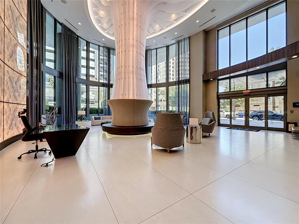 A modern lobby features a central sculptural column, floor-to-ceiling windows, and tile flooring — 100 1ST AVENUE N UNIT 1106, ST PETERSBURG, FL