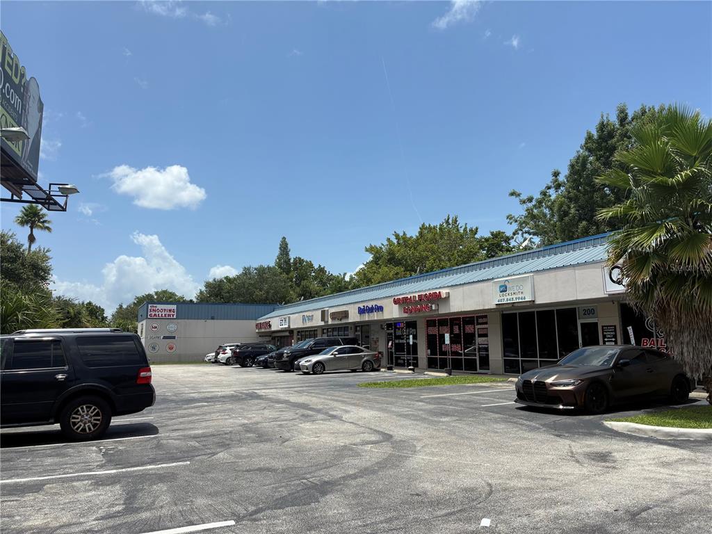 A parking lot sits in front of a single-story commercial strip mall under a blue sky — 2911 39TH STREET UNIT 200, ORLANDO, FL
