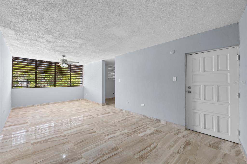 An empty room with light gray walls, marble-look tile flooring, and a large window — 3015 ALMONTE ST. COND. GUARIONEX APT. 304, SAN JUAN, PR