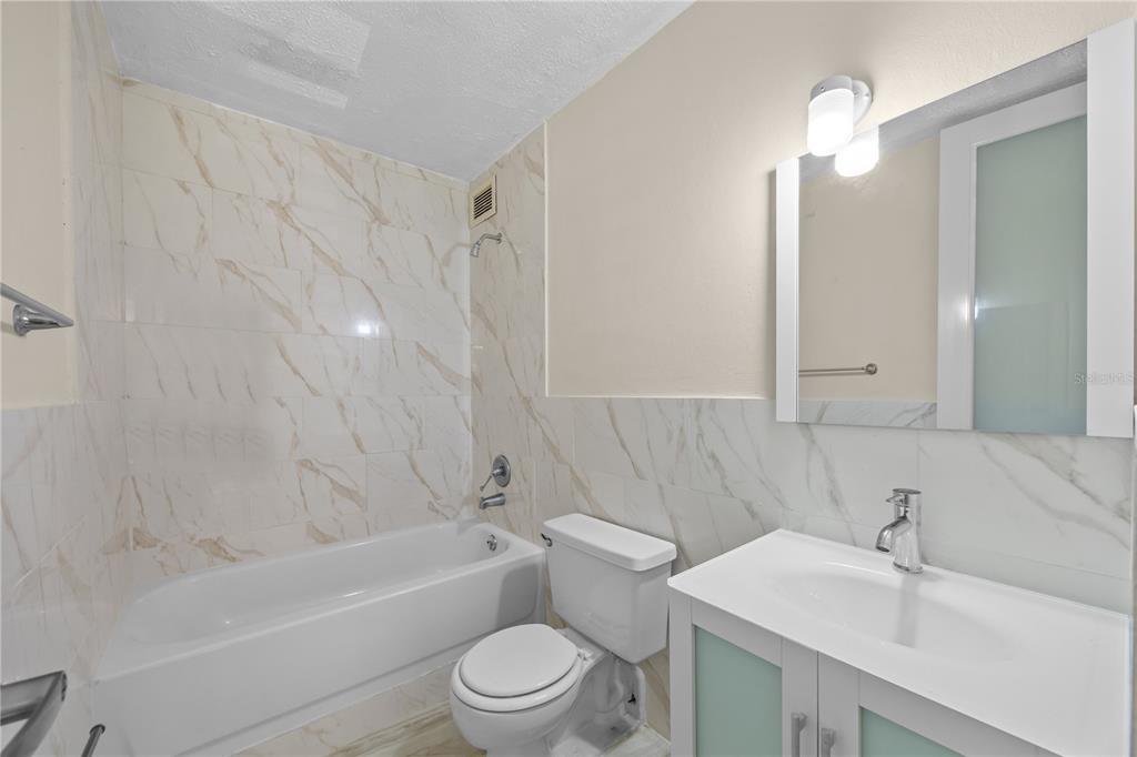 A bathroom features a white vanity, a toilet, and a bathtub with marble-patterned tile walls — 3015 ALMONTE ST. COND. GUARIONEX APT. 304, SAN JUAN, PR