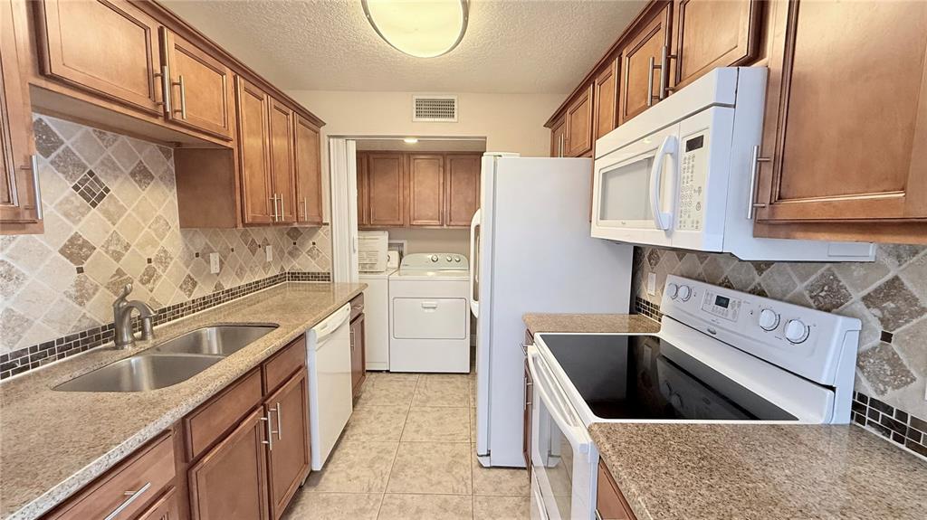 A galley-style kitchen features wood cabinets, granite countertops, tile backsplashes, and white appliances — 524 ORANGE DRIVE UNIT 11, ALTAMONTE SPRINGS, FL