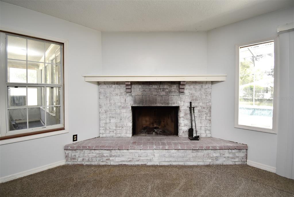 A corner brick fireplace with a white mantel sits between two windows in a carpeted room — 5133 BRENDA DRIVE, ORLANDO, FL