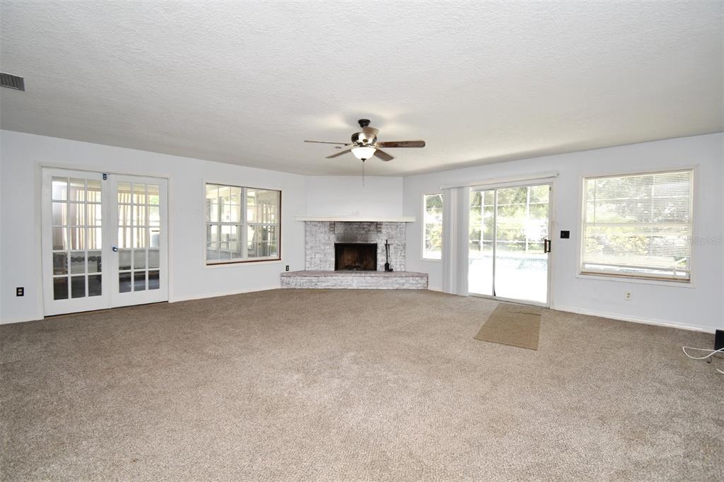 A spacious living room features beige carpet, a white brick corner fireplace, and sliding glass doors — 5133 BRENDA DRIVE, ORLANDO, FL