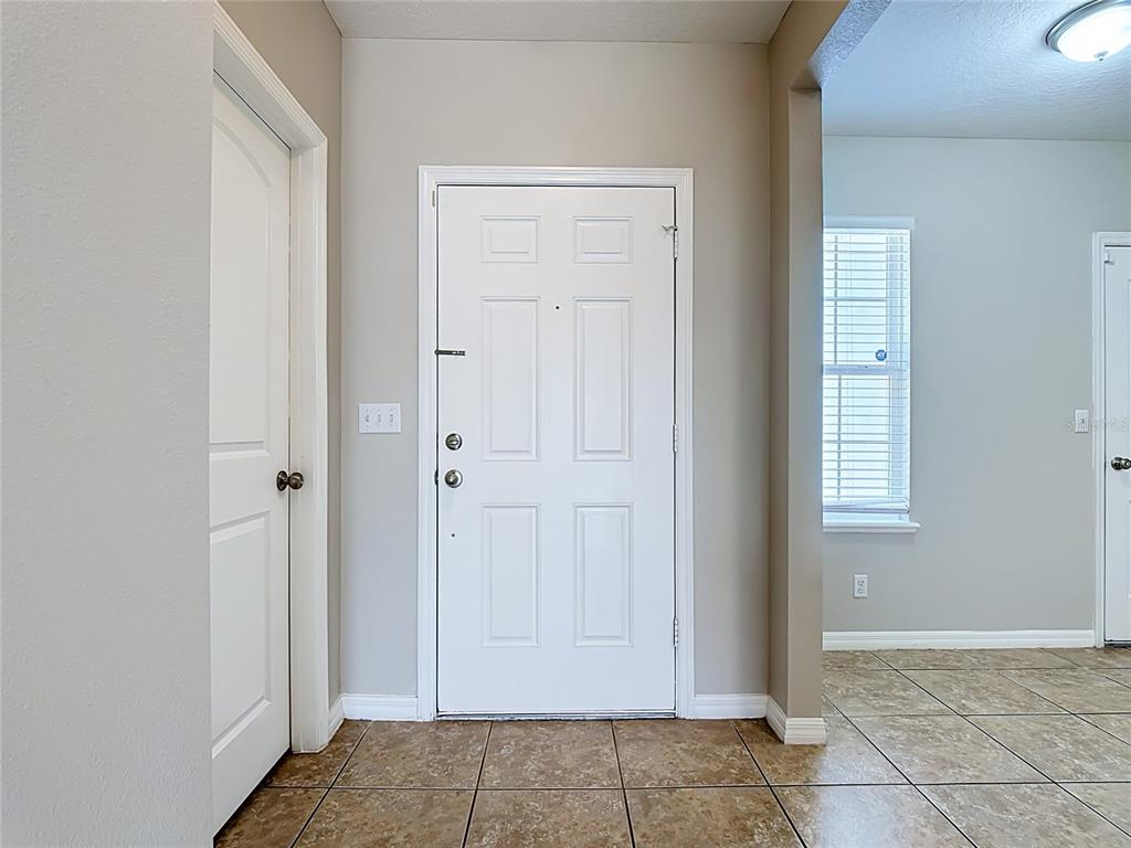 An entryway features a white front door, tiled flooring, and a doorway to an adjacent room — 1562 TAMARIND ROAD, DAVENPORT, FL