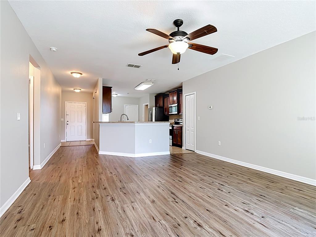 An open-concept living area features wood-look flooring, a ceiling fan, and a kitchen with cabinets — 1562 TAMARIND ROAD, DAVENPORT, FL