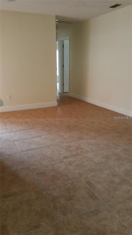 An interior view of a room with light-colored walls and brown tiled flooring — 503 PINE BARK COURT, KISSIMMEE, FL