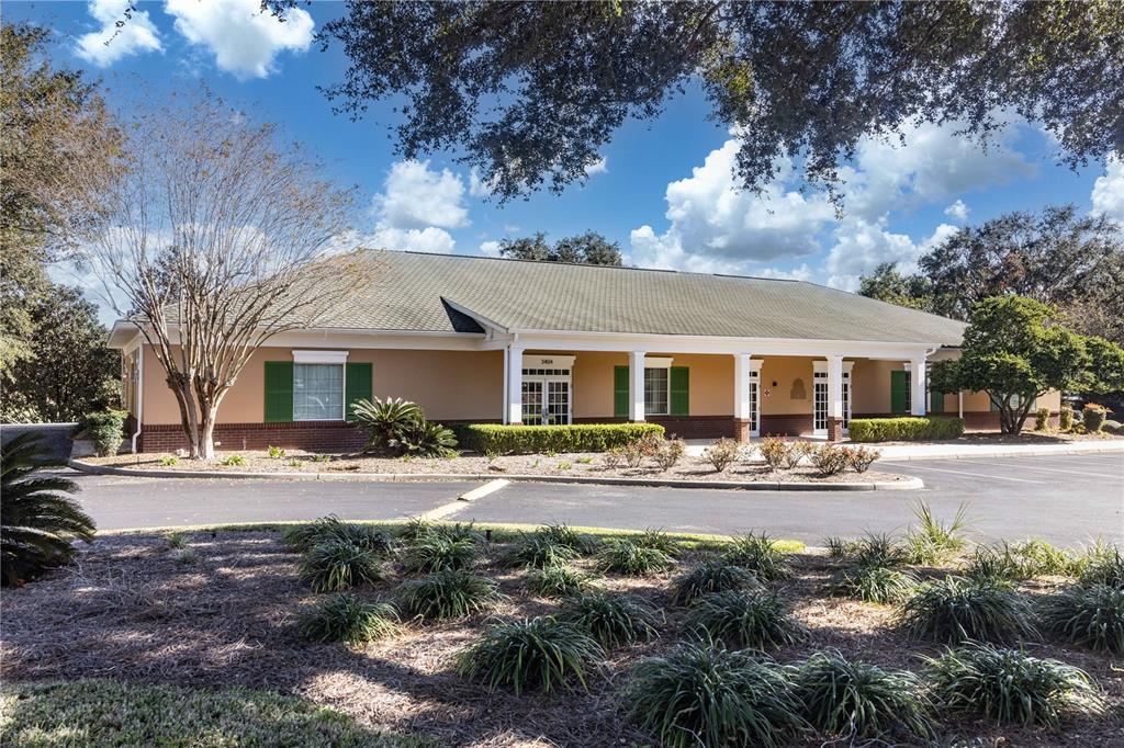 A single-story commercial building with a covered walkway, green shutters, and a paved parking lot — 3400 SOUTHERN TRACE, THE VILLAGES, FL