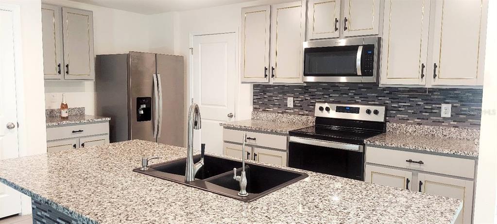 A kitchen features a granite island, stainless steel appliances, and light-colored cabinetry with gold trim — 35386 SPRUCE KNOB COURT, DADE CITY, FL