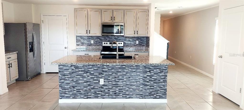 A kitchen features a granite-topped island, gray tiled backsplash, stainless steel appliances, and light cabinetry — 35386 SPRUCE KNOB COURT, DADE CITY, FL