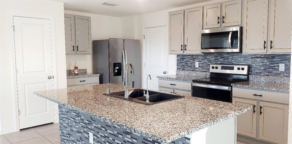 A kitchen features a granite-topped island, gray cabinets with gold trim, and stainless steel appliances — 35386 SPRUCE KNOB COURT, DADE CITY, FL