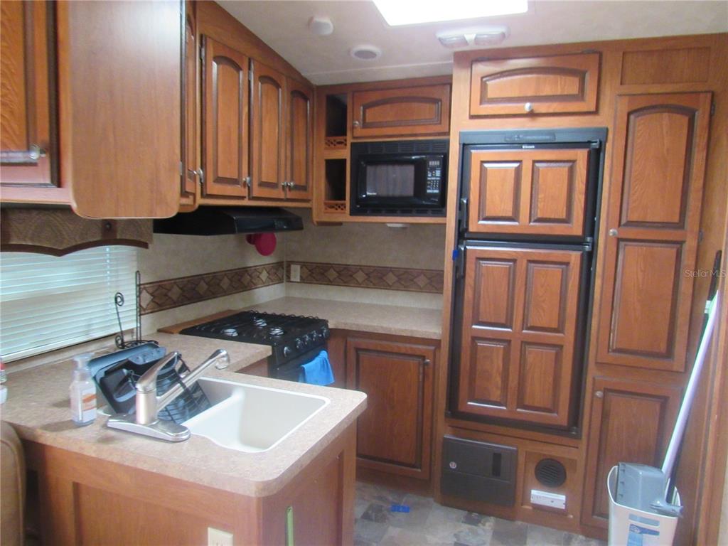 A kitchen in a recreational vehicle features wood cabinetry, a microwave, a stove, and a refrigerator — 1950 SE 185TH TERRACE, SILVER SPRINGS, FL