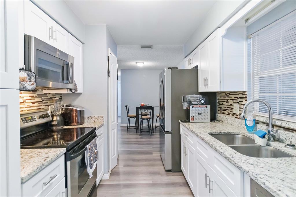A galley kitchen features white cabinets, granite countertops, stainless steel appliances, and a dining area — 1115 S ALDER AVENUE, ORLANDO, FL