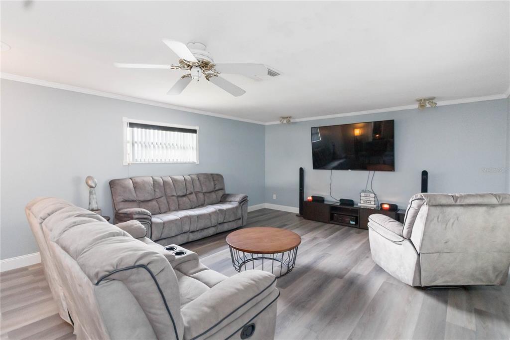 A living room features light blue walls, gray wood-look flooring, a ceiling fan, and furniture — 1115 S ALDER AVENUE, ORLANDO, FL