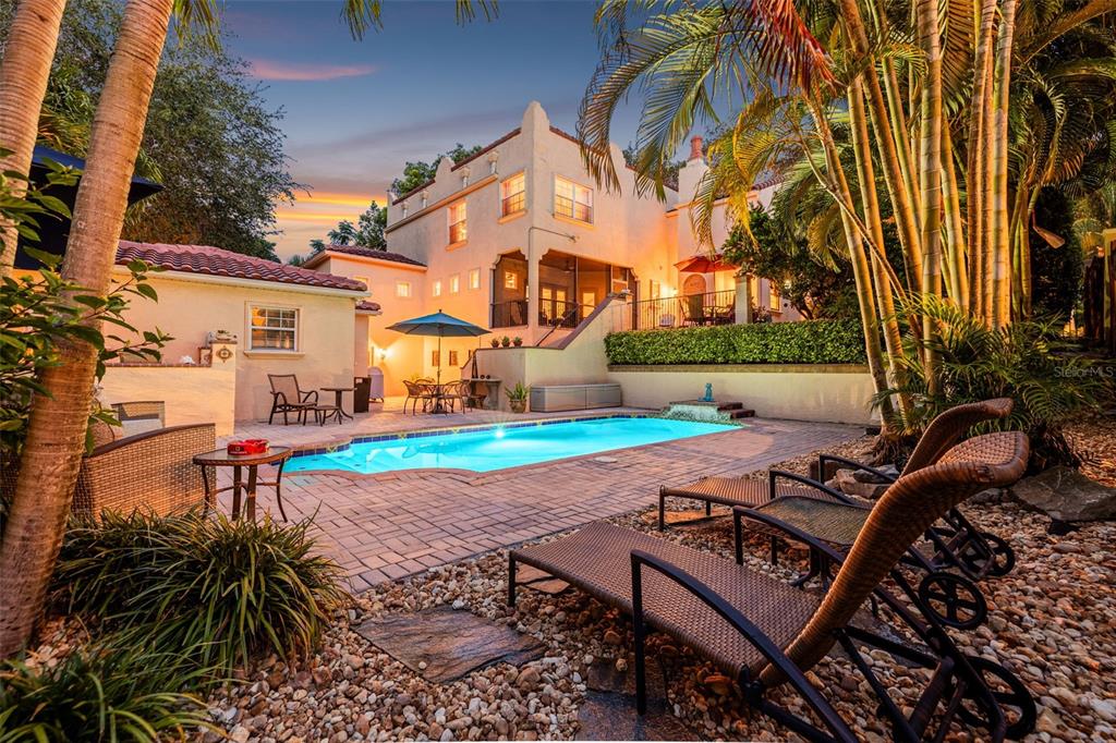 A backyard swimming pool with a patio and lounge chairs sits before a multi-story house — 322 ROEBLING ROAD S, BELLEAIR, FL