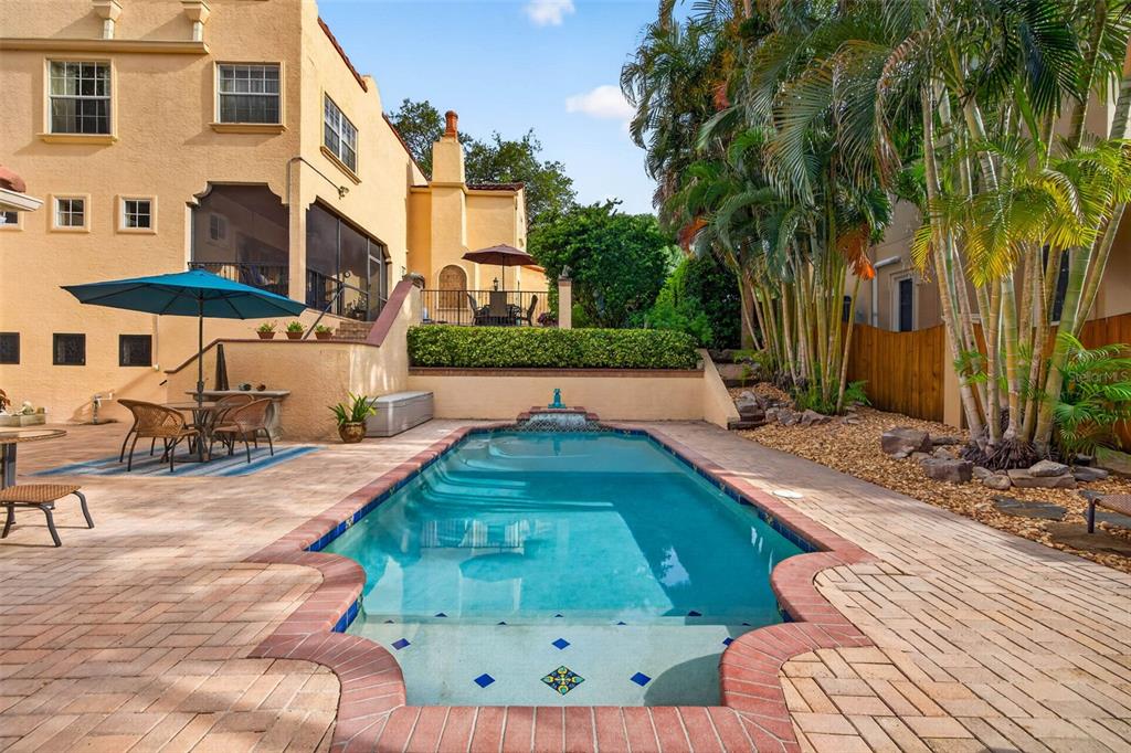 A swimming pool with a brick border sits on a patio next to a house — 322 ROEBLING ROAD S, BELLEAIR, FL