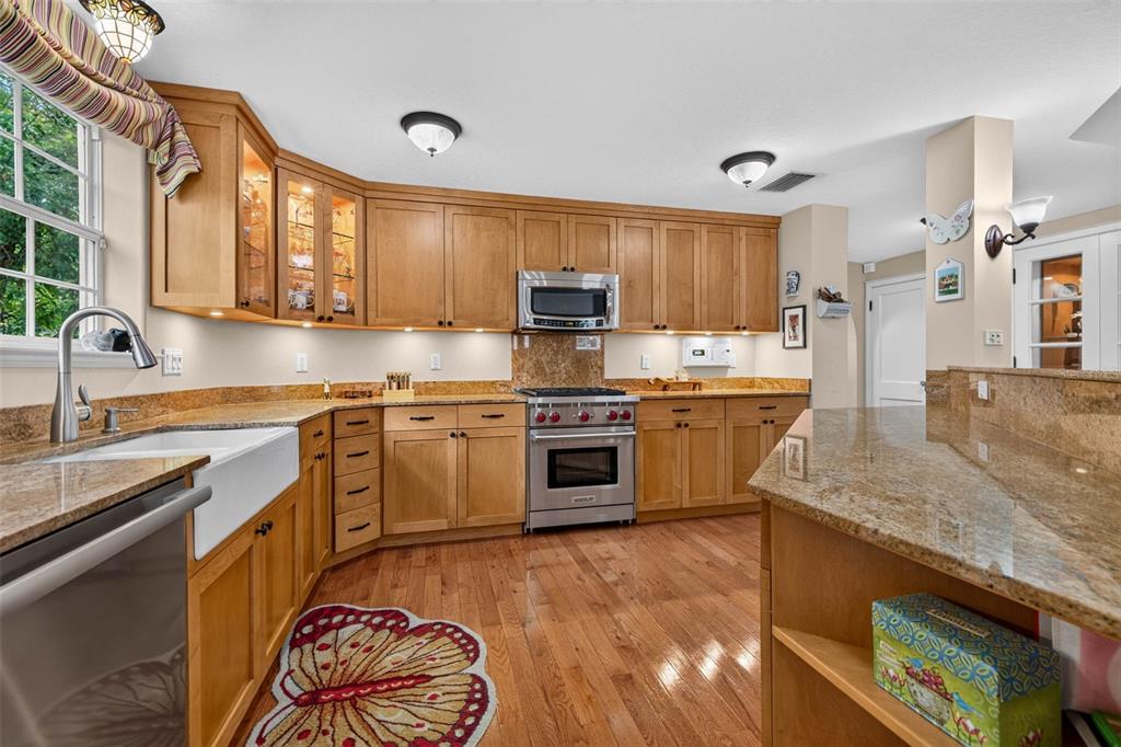 A kitchen features light wood cabinets, granite countertops, a farmhouse sink, and hardwood flooring — 322 ROEBLING ROAD S, BELLEAIR, FL