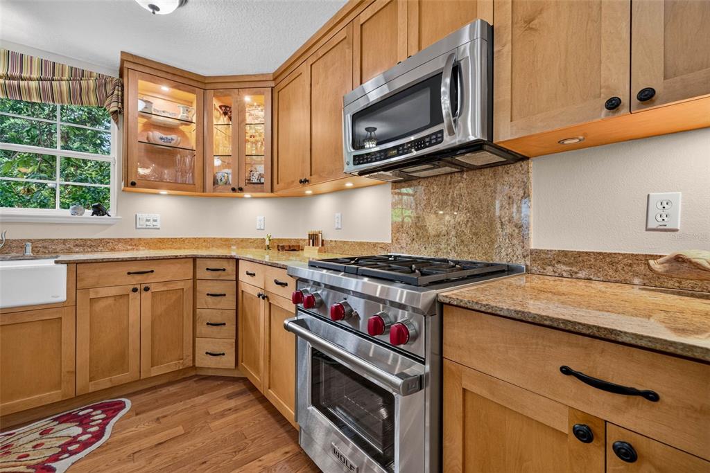 A kitchen features light wood cabinets, granite countertops, a stainless steel gas range, and microwave — 322 ROEBLING ROAD S, BELLEAIR, FL