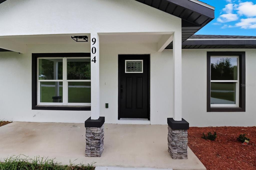 A white house exterior features a black front door, dark window frames, and stone pillars — 19857 SW FLAMINGO DRIVE, DUNNELLON, FL