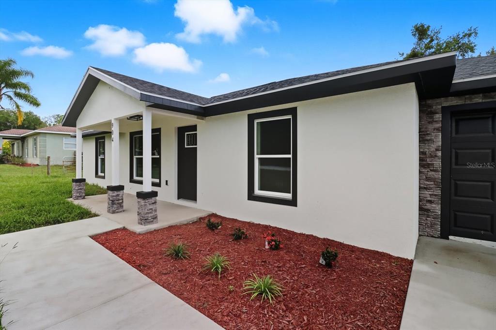 A white house exterior features a covered porch with stone-based columns and dark trim — 19857 SW FLAMINGO DRIVE, DUNNELLON, FL