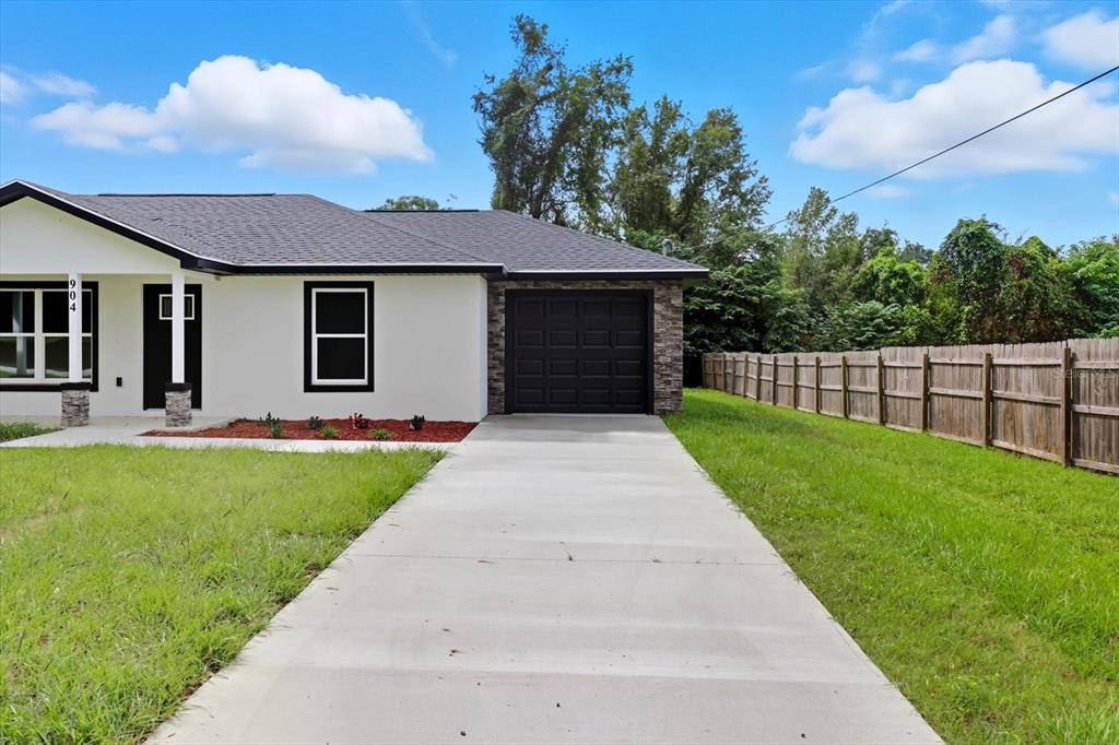 A white house with a black garage door and a concrete driveway sits on a lawn — 19857 SW FLAMINGO DRIVE, DUNNELLON, FL