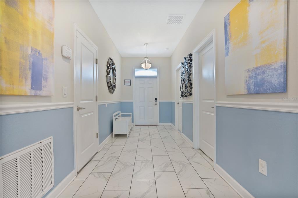 A bright entryway features white tile floors, blue wainscoting, and two large abstract paintings — 1613 MAIDSTONE COURT, DAVENPORT, FL