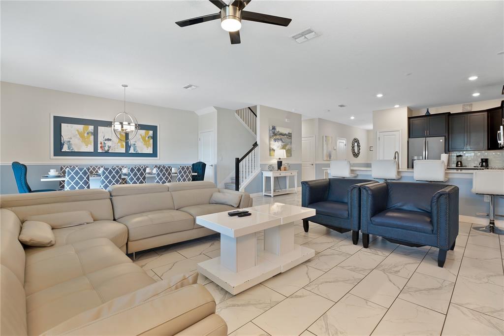 An open-concept living and dining area features a large sectional, blue armchairs, and tile flooring — 1613 MAIDSTONE COURT, DAVENPORT, FL