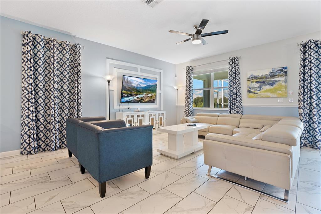 A living room features a white sectional sofa, blue armchairs, and a wall-mounted television — 1613 MAIDSTONE COURT, DAVENPORT, FL