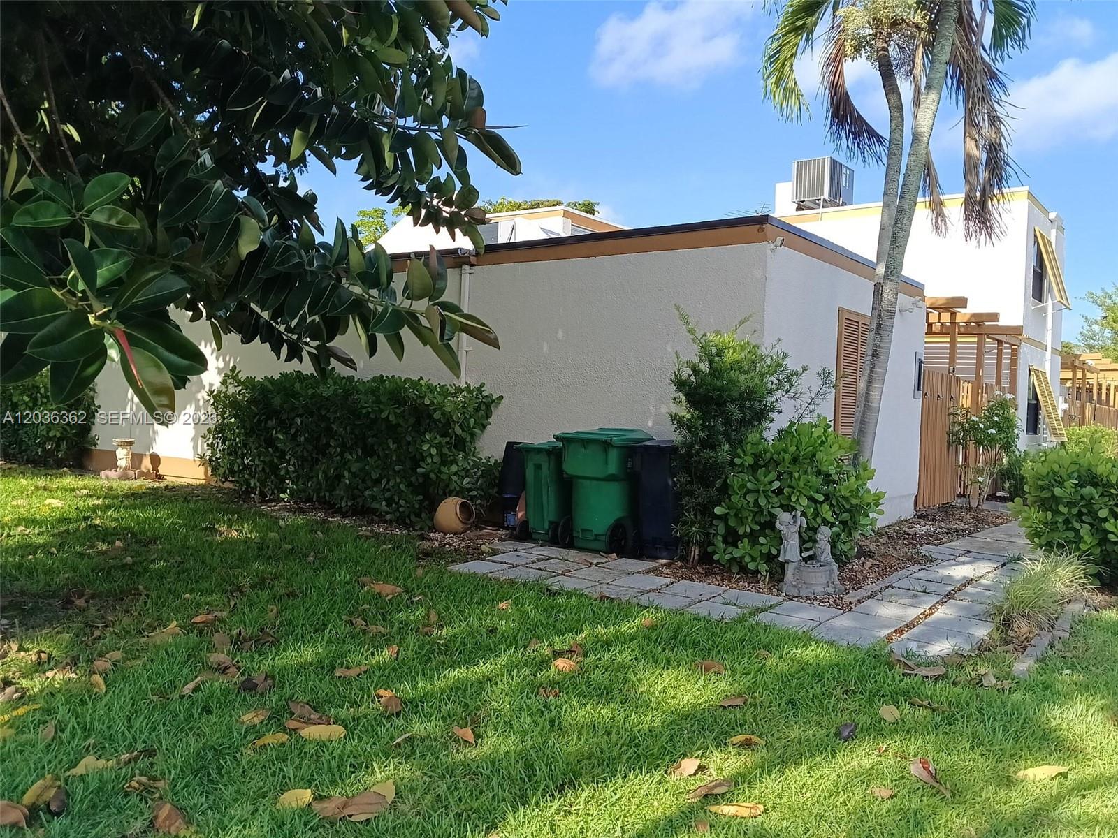A side view of a stucco building with green trash bins and landscaping — 1700 SW 131st Place Cir S, Miami FL 33175, MIAMI, FL