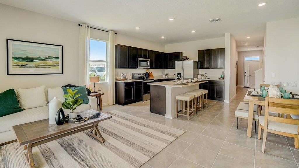 An open-concept living room and kitchen featuring dark cabinetry, a center island, and tile flooring — 31243 PAPER BIRCH STREET, WESLEY CHAPEL, FL