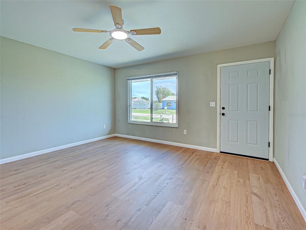 An empty room features light wood-look flooring, a ceiling fan, a window, and a door — 6837 KETONA ROAD, NORTH PORT, FL