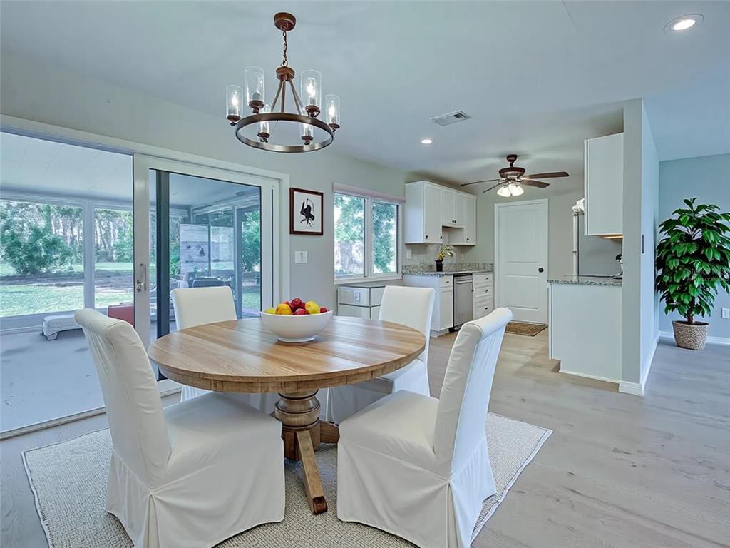 A dining area features a round wooden table, white slipcovered chairs, and a chandelier — 6837 KETONA ROAD, NORTH PORT, FL
