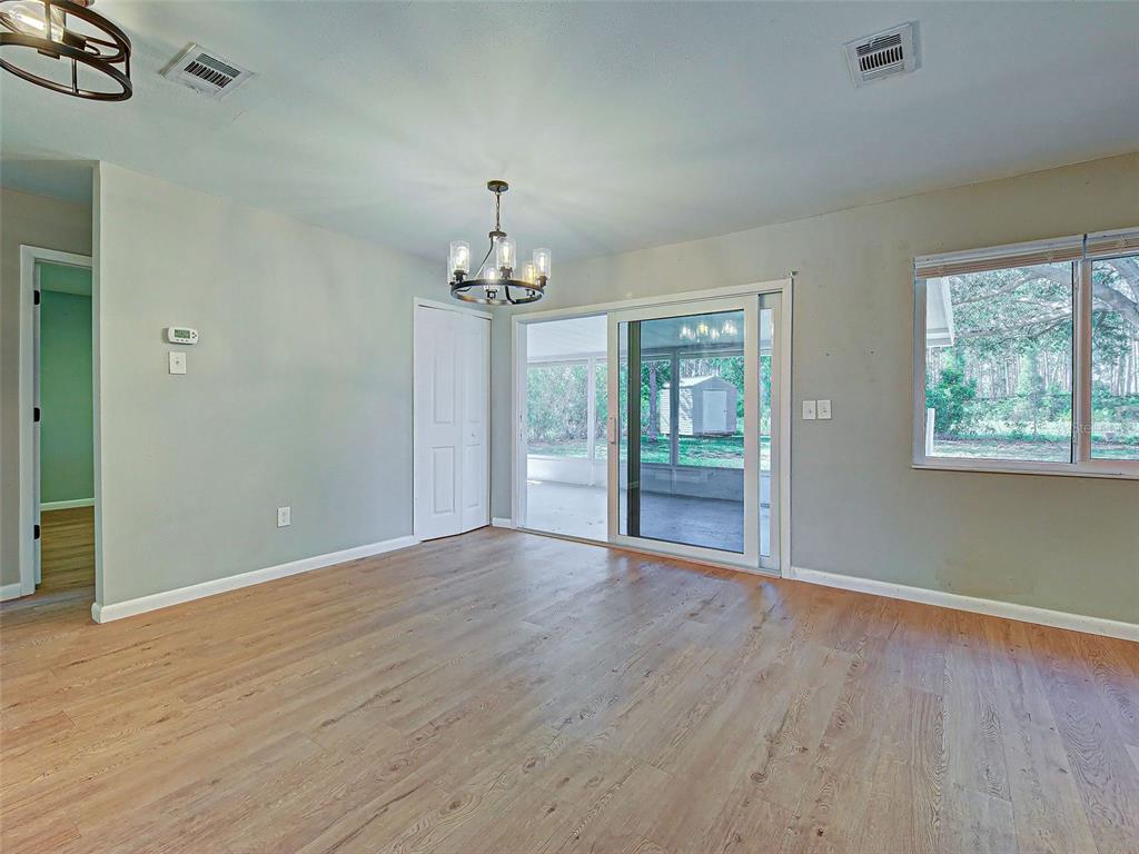 A dining area features wood-look flooring, a chandelier, a sliding glass door, and a window — 6837 KETONA ROAD, NORTH PORT, FL