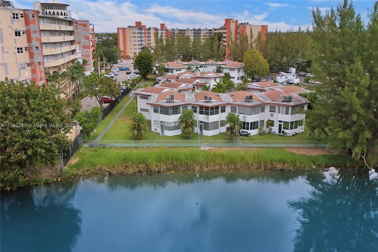 An aerial view shows a multi-unit residential complex with red roofs situated beside a lake — 18746 NE 18th Ave # 146, Miami FL 33179, MIAMI, FL