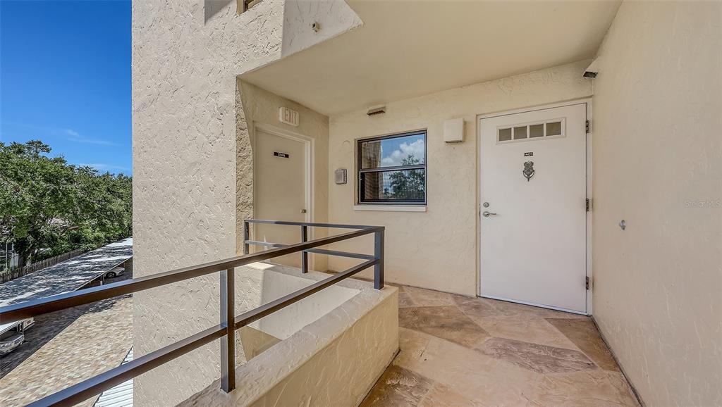 An outdoor apartment balcony features a tiled floor, a metal railing, and two white doors — 8779 MIDNIGHT PASS ROAD UNIT 401H, SARASOTA, FL