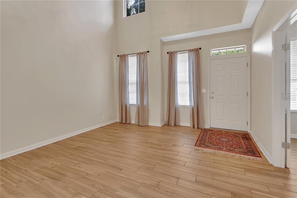 An empty room with high ceilings, light wood-look flooring, two windows with curtains, and a door — 204 WOODHOUSE LANE, DELAND, FL