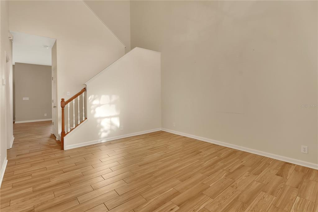 An empty room with light wood-look flooring, a high ceiling, and a wooden staircase — 204 WOODHOUSE LANE, DELAND, FL