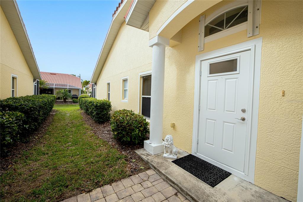 A white front door with a transom window sits beside a column on a paved porch — 3799 ALBACETE CIRCLE UNIT 65, PUNTA GORDA, FL