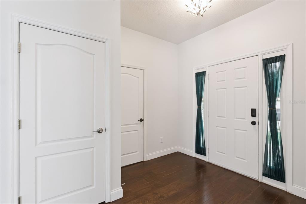 An entryway with dark wood floors, white walls, two interior doors, and a front door — 1008 MAGNOLIA BLOSSOM COURT, APOPKA, FL
