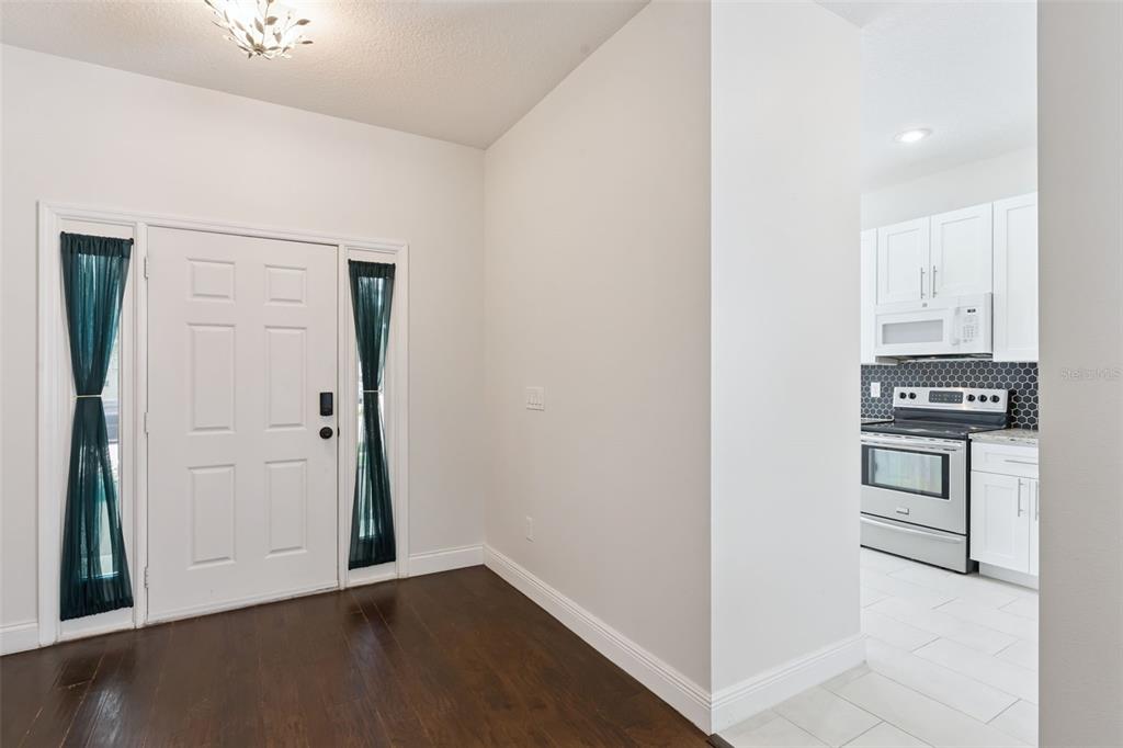 An entryway with dark wood floors leads to a kitchen with white cabinets and appliances — 1008 MAGNOLIA BLOSSOM COURT, APOPKA, FL