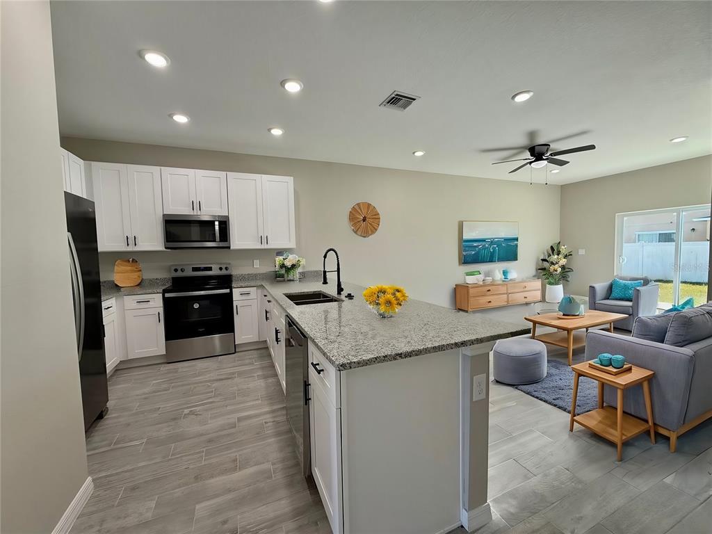 A modern kitchen with white cabinets and granite countertops opens into a living room area — 721 BITTERN LANE UNIT A, POINCIANA, FL