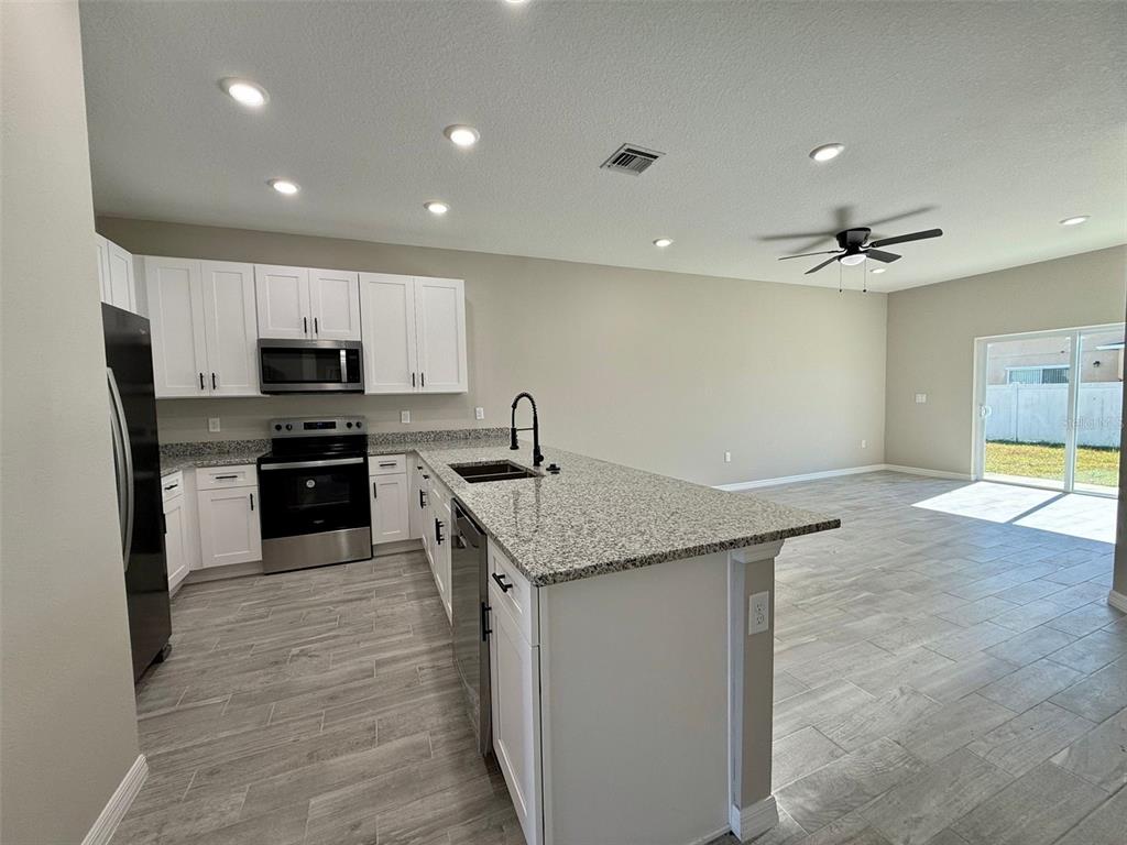 A kitchen with white cabinets, granite countertops, and stainless steel appliances opens to a living area — 721 BITTERN LANE UNIT A, POINCIANA, FL