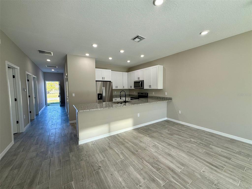 A kitchen with white cabinets, granite countertops, and tile flooring opens to a living area — 721 BITTERN LANE UNIT A, POINCIANA, FL