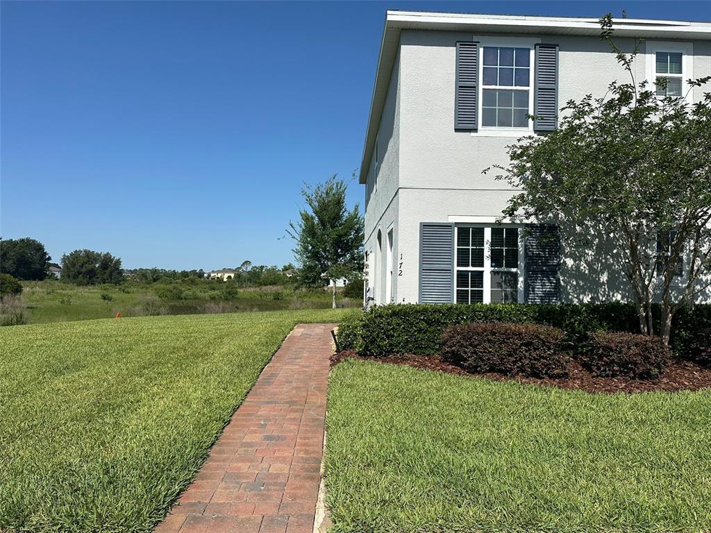 A brick walkway leads to the side entrance of a two-story house with gray siding — 172 PRIMROSE DRIVE, DAVENPORT, FL