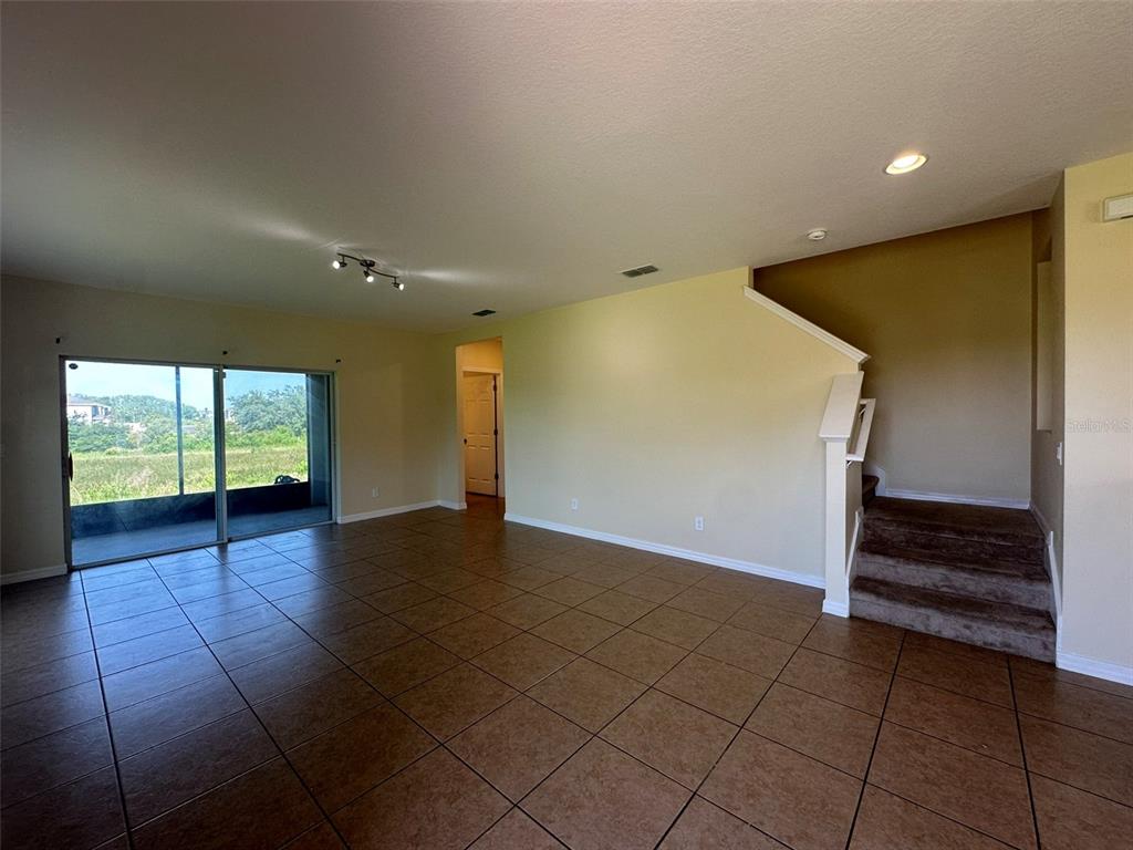 An open living area features tan tile flooring, a staircase, and sliding glass doors — 172 PRIMROSE DRIVE, DAVENPORT, FL