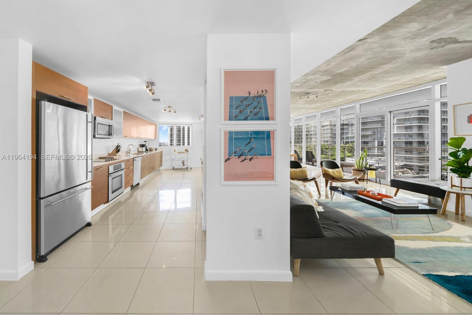 A modern kitchen with wood cabinets and tile floors opens into a bright living area — 3250 NE 1st Ave # 1104, Miami FL 33137, MIAMI, FL