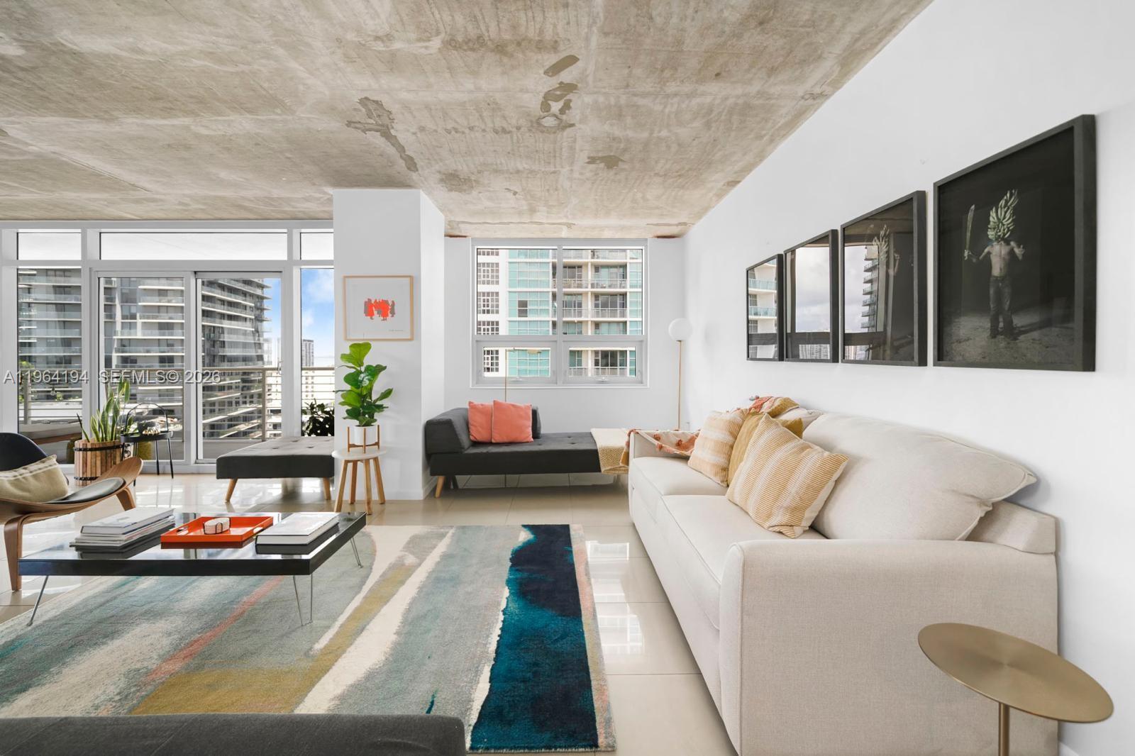 A modern living room features a concrete ceiling, a large area rug, and floor-to-ceiling windows — 3250 NE 1st Ave # 1104, Miami FL 33137, MIAMI, FL